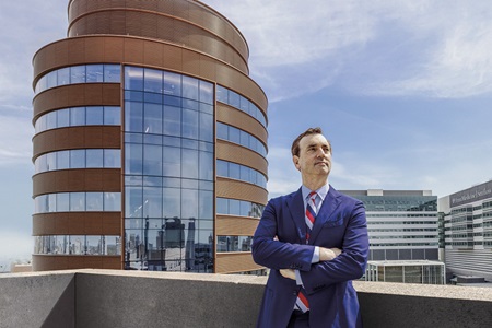 Daniel Yoshor, MD, chair of Neurosurgery, stands with his arms folded, looking off to the distance, on the roof of HUP's Silverstein building, with the Pavilion in the background.